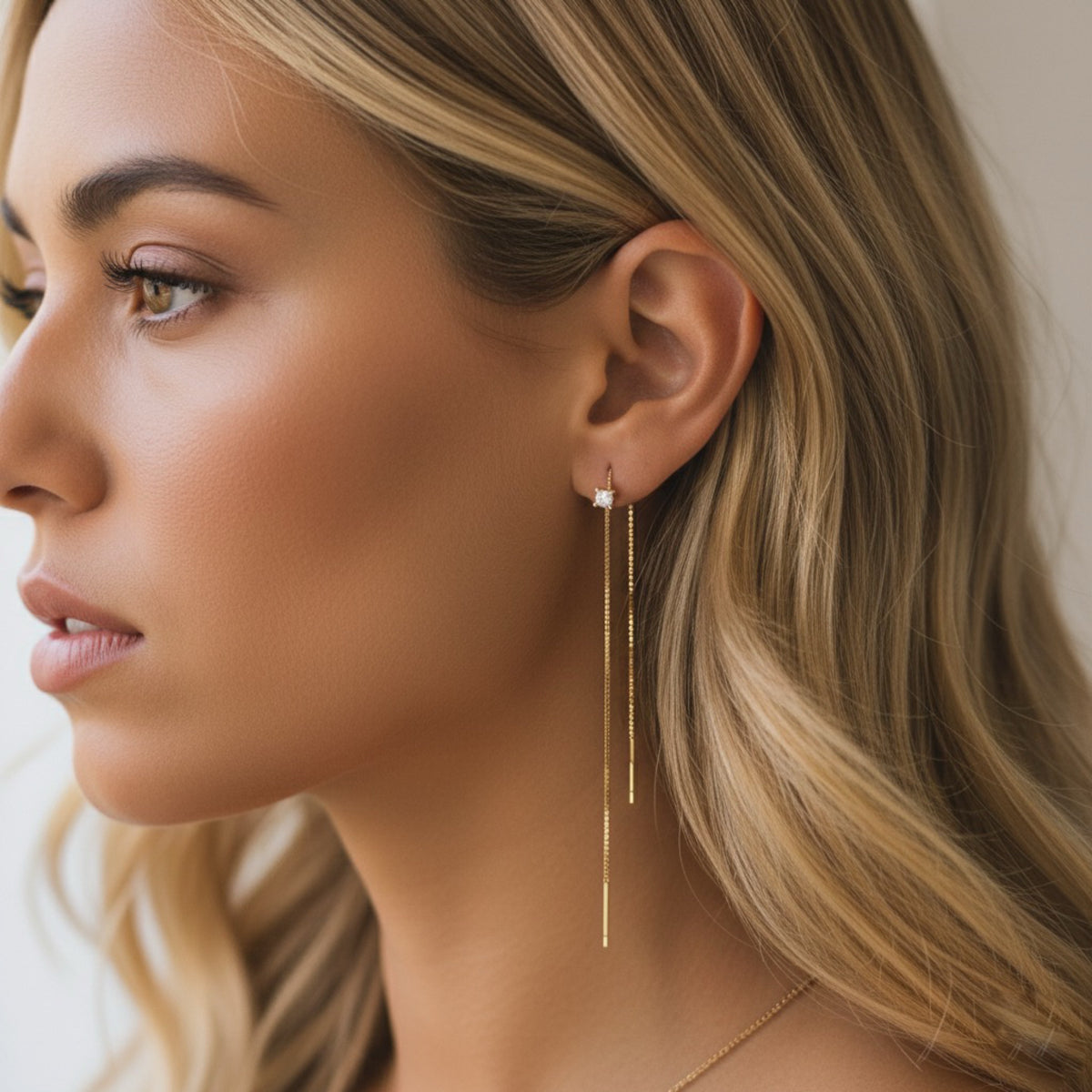Close-up of a woman wearing gold threader  earrings with a neutral background