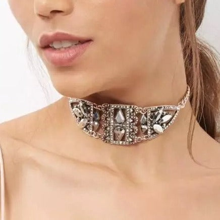A close-up image of a woman wearing a silver-colored metal choker necklace adorned with rhinestones.