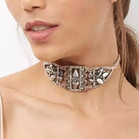 A close-up image of a woman wearing a silver-colored metal choker necklace adorned with rhinestones.