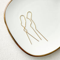 A pair of Adara Threader Earrings featuring a minimalist chain design, displayed on a white plate with a gold rim.