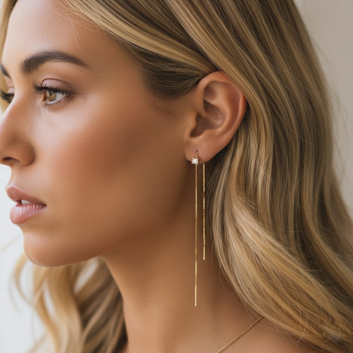 Close-up of a woman wearing gold threader  earrings with a neutral background