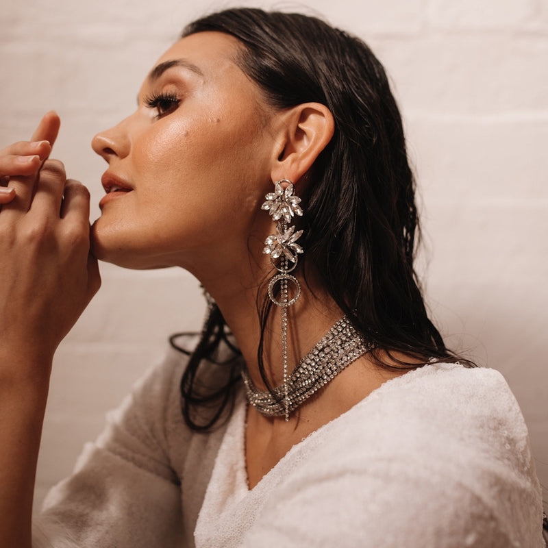 A woman wearing a white top and earrings with a floral motif and cascading chains of rhinestones.