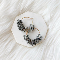 Hoop earrings with gray floral accents on a white hexagonal stand against a white background. Anielle Flower Hoops Earrings - The Songbird Collection - 