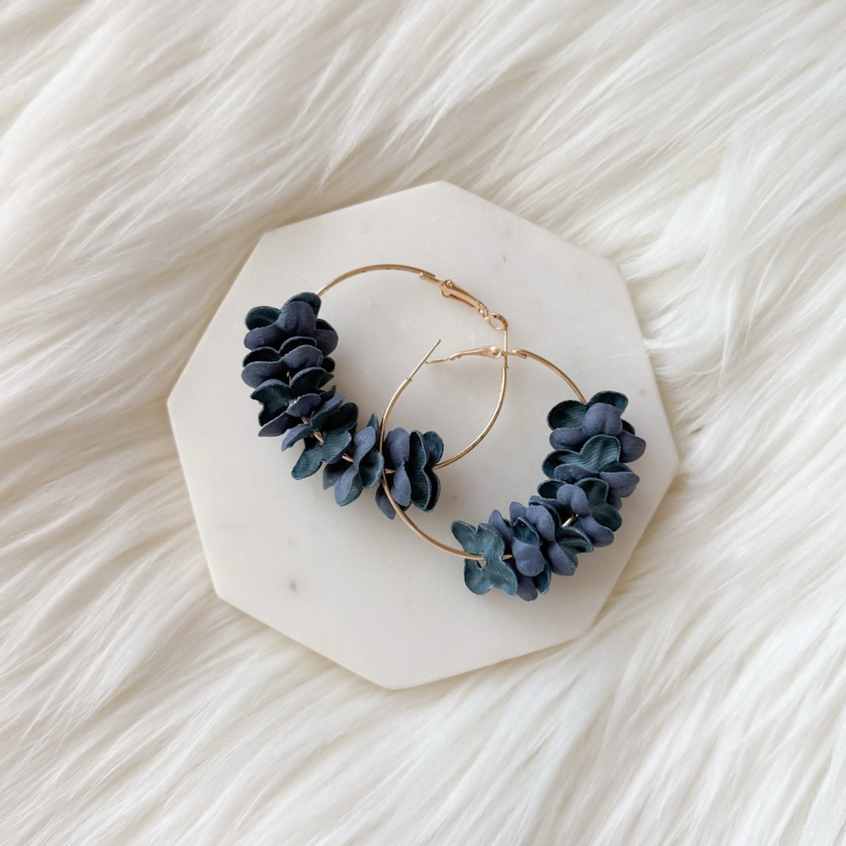 Gold hoop earrings with blue stone accents on a white marble stand. Anielle Flower Hoops Earrings - The Songbird Collection - 