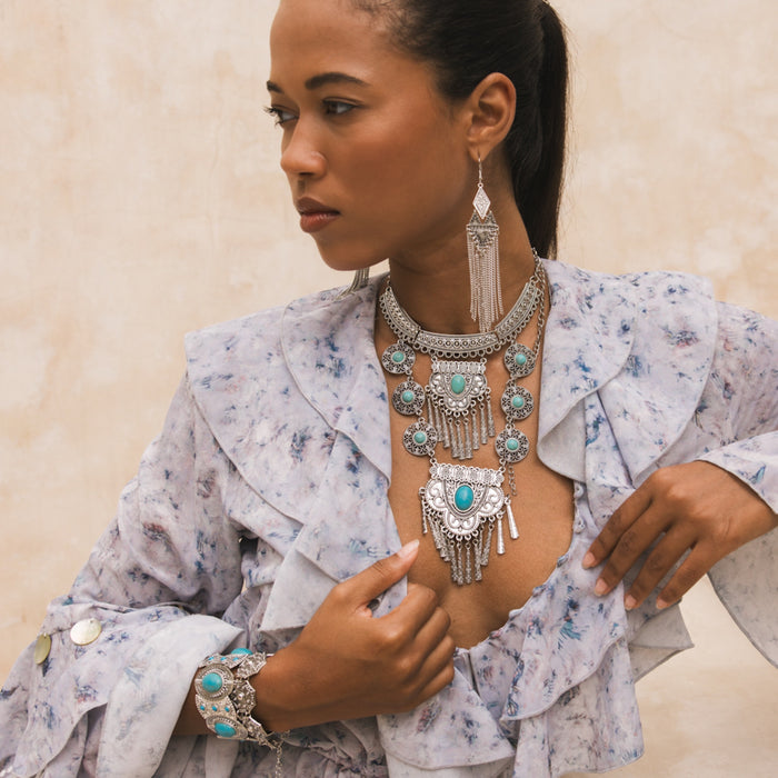 Woman wearing a detailed silver and turquoise jewelry set against a neutral background