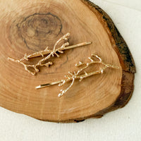 Two gold branch-shaped hair pins displayed on a rustic wood slice background.  Arbors Hair Pin Set - The Songbird Collection