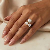 Hand wearing a ring with pearls and a diamond on a neutral background