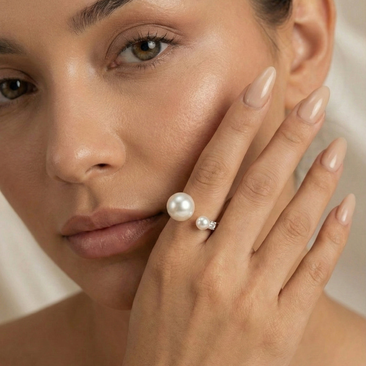 Close-up of a woman's face with a pearl earring and ring on a neutral background