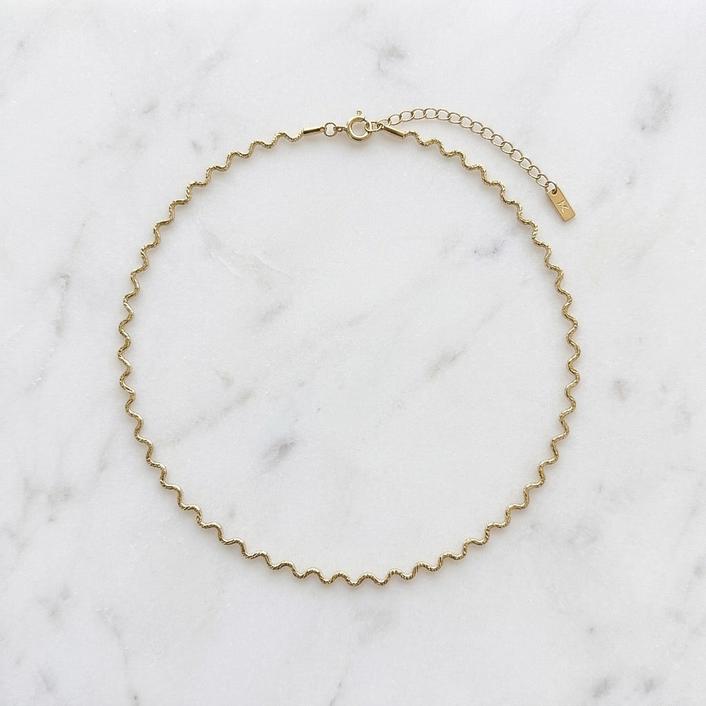 Gold wavy chain necklace on a marble surface - Aura Ripple Chain Necklace - The Songbird Collection