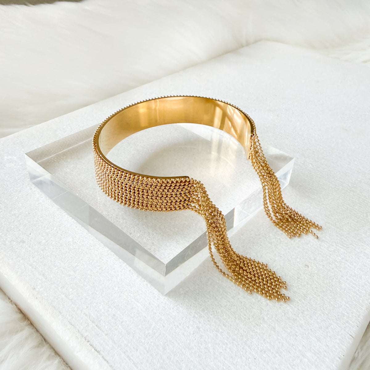 Gold beaded cuff with tassels on a white surface