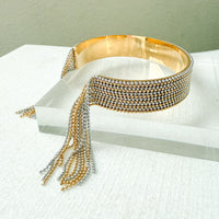 Gold beaded cuff bracelet on a white surface with a light green background