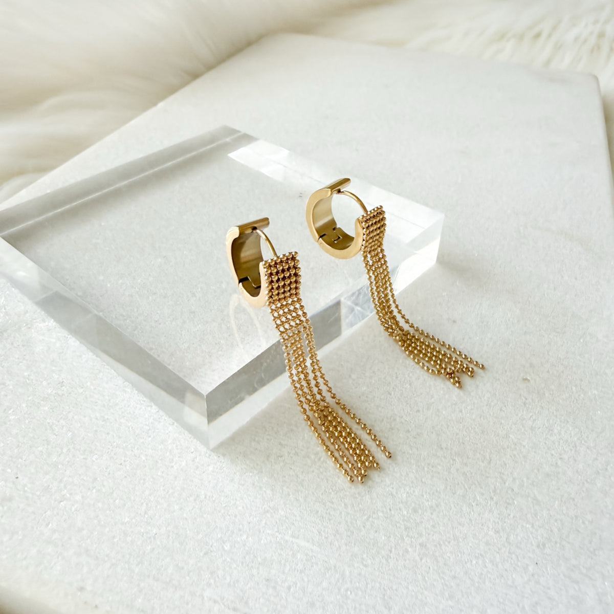 Gold hoop earrings with tassel details on a white surface