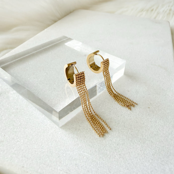 Gold hoop earrings with tassel details on a white surface
