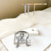 Silver fringe earrings, matching bracelet, and ring on a gold earring stand with a white fur surface.