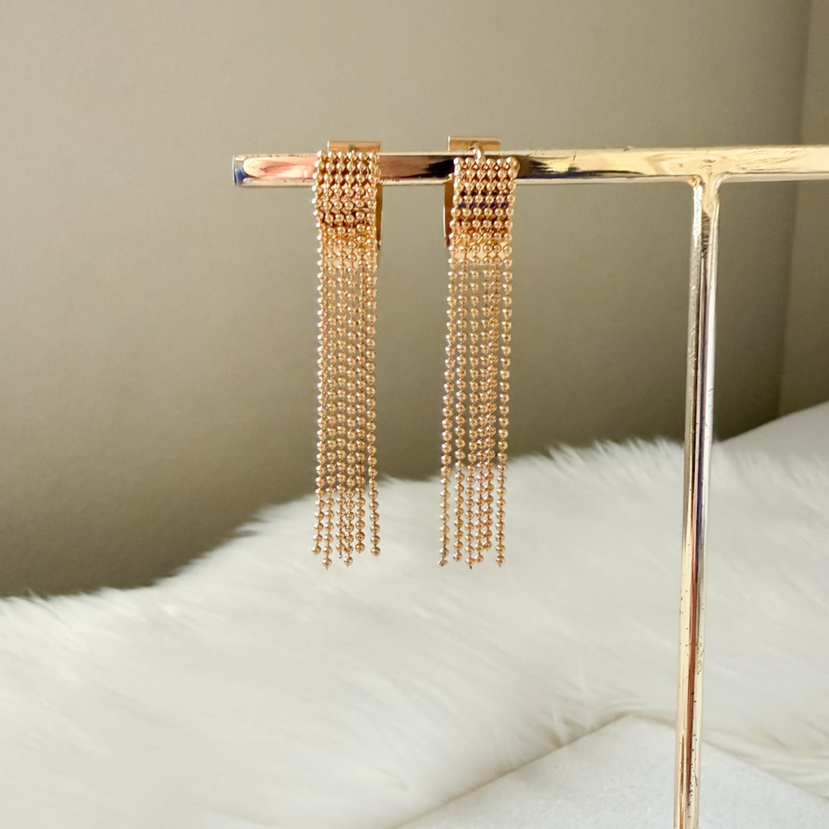 Gold chain earrings on a stand with a neutral background