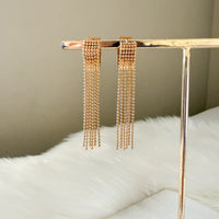 Gold chain earrings on a stand with a neutral background