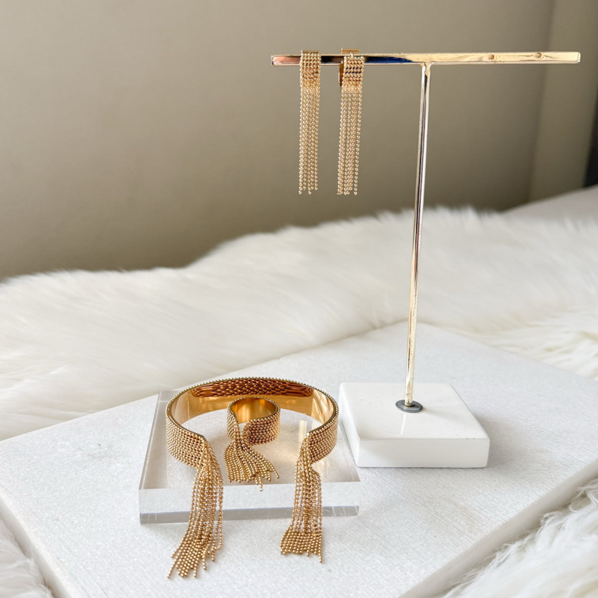 Gold jewelry set including earrings and a bracelet on a white surface with a neutral background