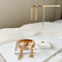 Gold jewelry set including earrings and a bracelet on a white surface with a neutral background