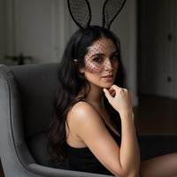 Woman wearing bunny ears and a black dress sitting on a chair.