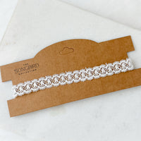 White lace choker on a brown cardboard holder with 'The Songbird Collection' branding.