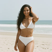 Woman in a white bikini standing on a beach with ocean in the background