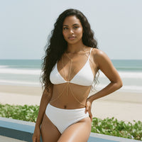 Woman in a white bikini standing on a beach with ocean in the background