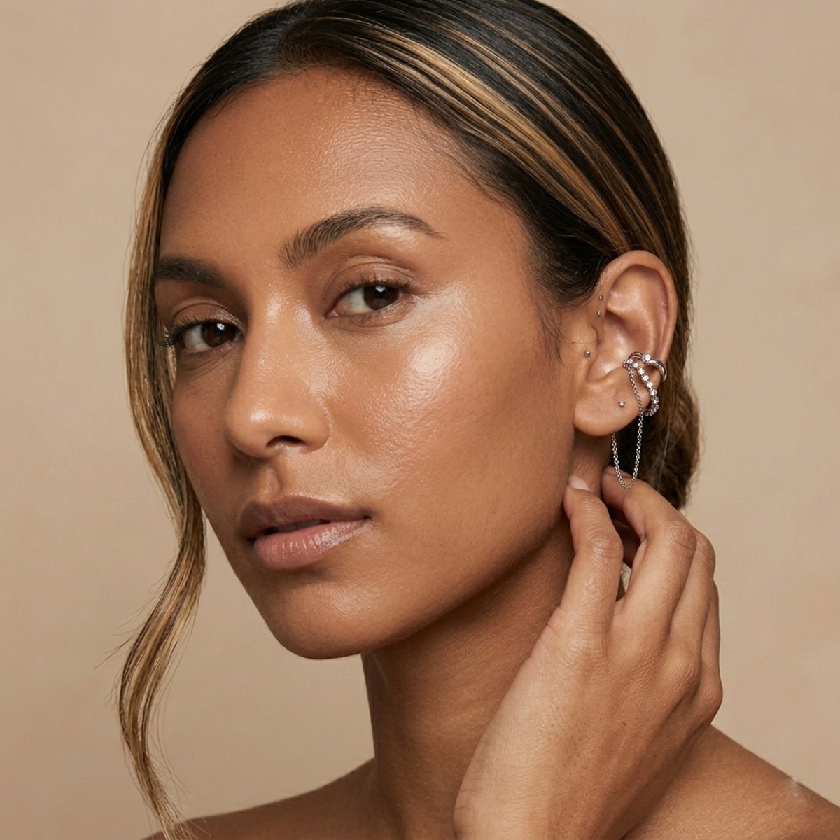 Woman adjusting an earring against a beige background - Cascading Chains Ear Cuff - The Songbird Collection