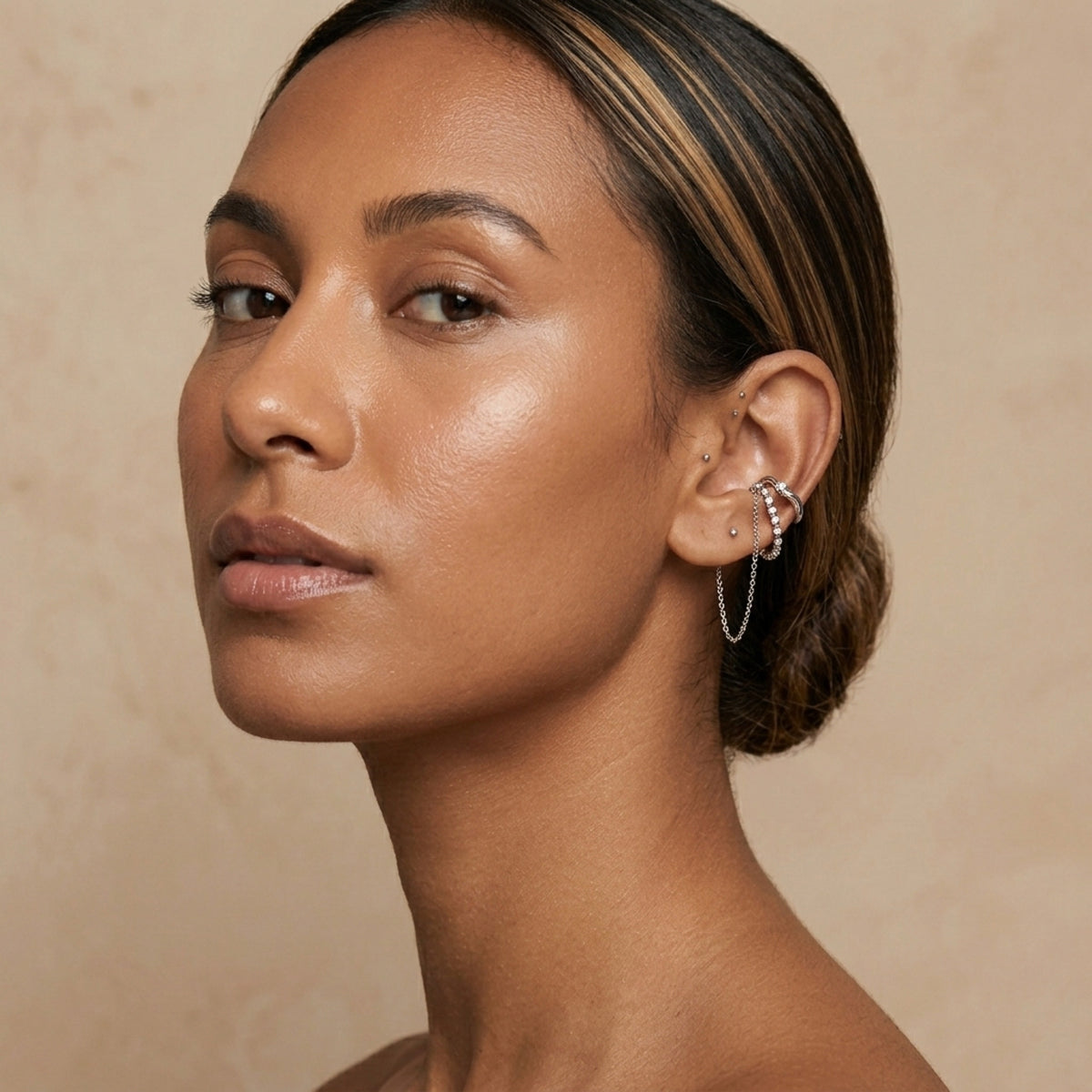 Close-up of a woman wearing earrings against a beige background. Cascading Chains Ear Cuff - The Songbird Collection