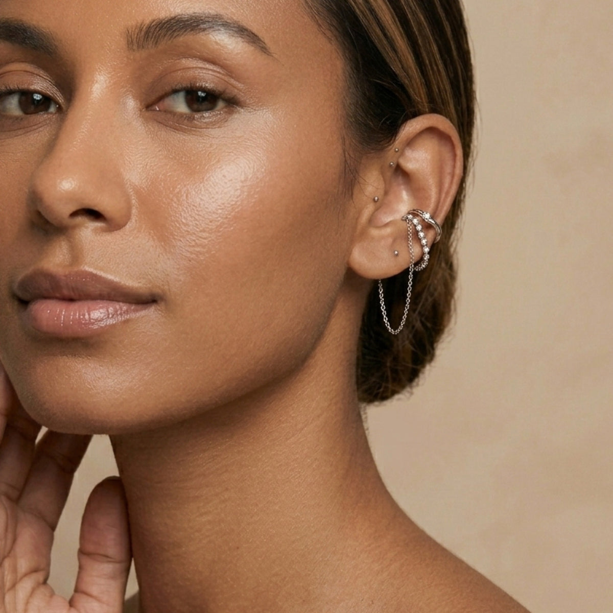 Close-up of a woman wearing multiple earrings with a neutral background. Cascading Chains Ear Cuff - The Songbird Collection