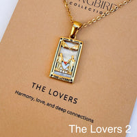 Gold pendant necklace with 'The Lovers' design on a brown card, featuring the brand 'The Songbird Collection'.