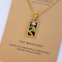 Gold necklace with 'The Magician' tarot card pendant on a beige card with text.