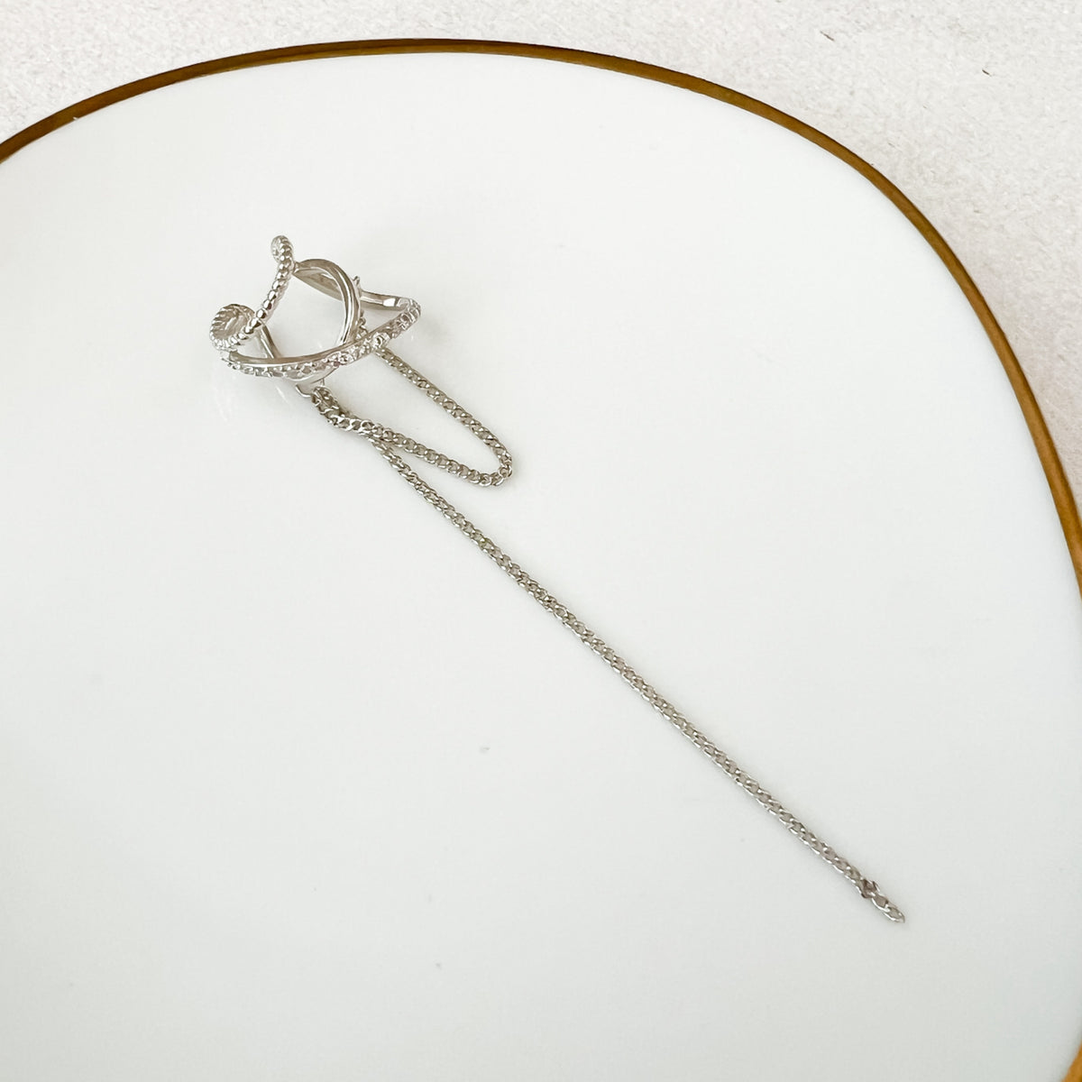 A silver ear cuff with a draping design and a hanging chain displayed on a white background.