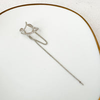A silver ear cuff with a draping design and a hanging chain displayed on a white background.