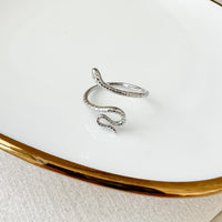 A gold-colored snake-shaped ring on a person's finger, showcasing a sleek and elegant design with a scale pattern.