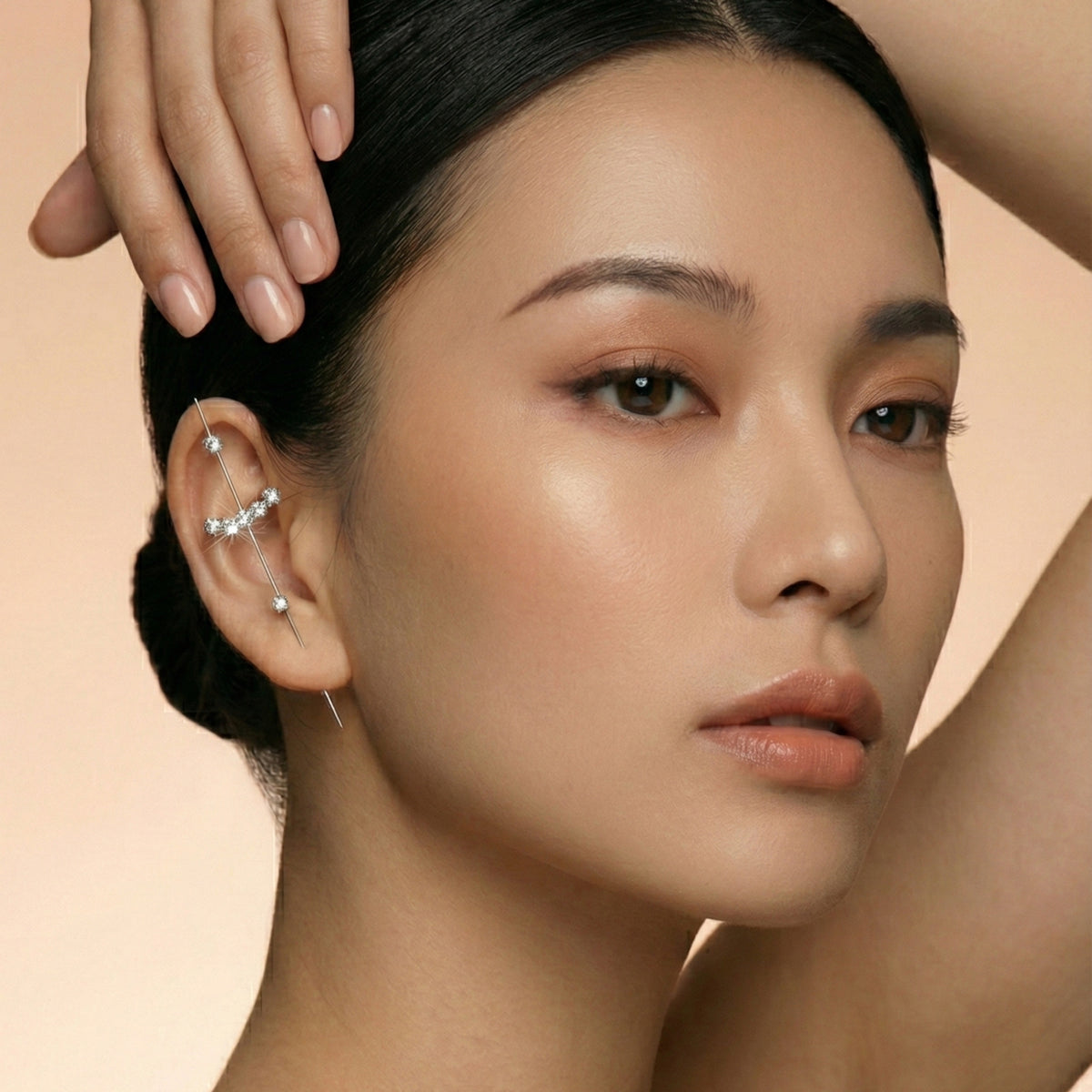 Close-up of a woman's face with a hand touching her hair against a beige background  Crystal_Bliss_Ear_Hook_Ear_Cuff-Earrings-The_Songbird_Collection
