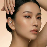 Close-up of a woman's face with a hand touching her hair against a beige background  Crystal_Bliss_Ear_Hook_Ear_Cuff-Earrings-The_Songbird_Collection