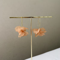 Pair of peach-colored flower earrings on a gold earring stand against a beige background.  Cyclamen Petal Drop Earrings - Chai Tea Latte - The Songbird Collection