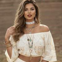 Woman wearing a white embroidered top with jewelry against a blurred natural background
