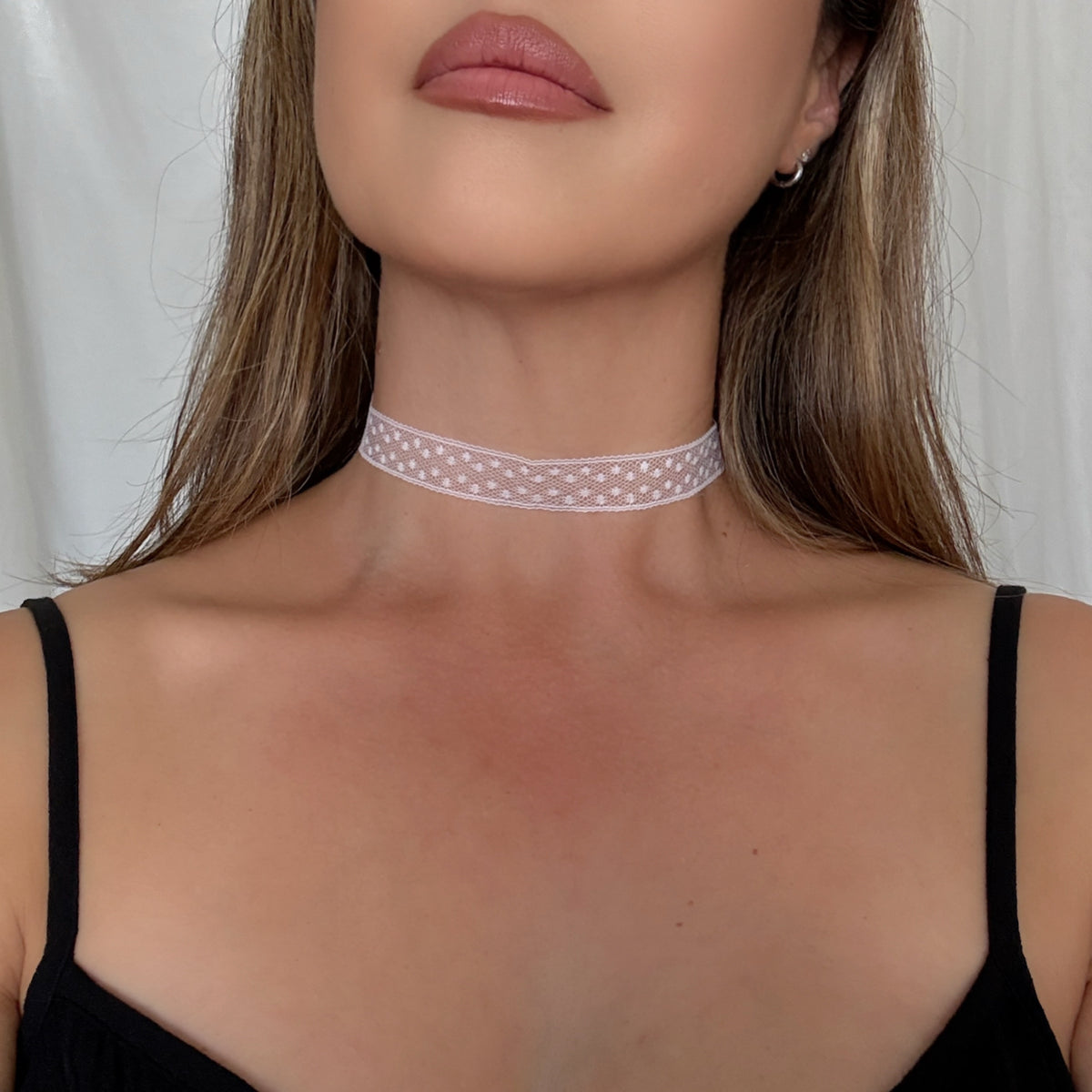 Woman wearing a delicate white lace choker against a neutral background
