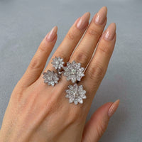 Hand wearing wrap around flower shaped rings on a gray background