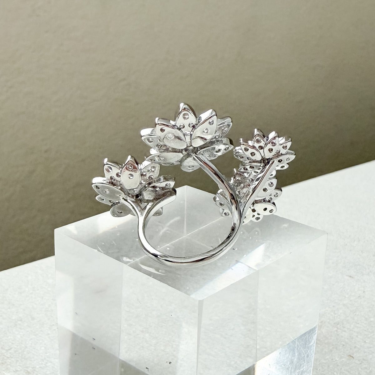 Silver ring with floral design on a white pedestal against a beige background