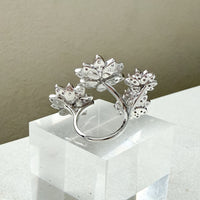 Silver ring with floral design on a white pedestal against a beige background