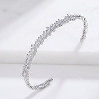 A silver-toned open cuff bracelet adorned with a continuous row of small clear marquise-cut stones, displayed on a white marble surface.  Esra Open Bangle - The Songbird Collection 
