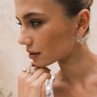 Close-up of a woman wearing butterfly earrings and a ring. The Songbird Collection