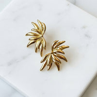 Gold leaf-shaped earrings on a white marble surface - Fireworks Statement Earrings - The Songbird Collection