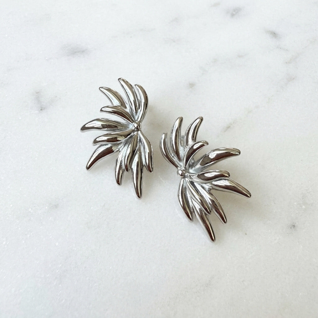 Pair of silver leaf-shaped earrings on a marble surface - Fireworks Statement Earrings - The Songbird Collection
