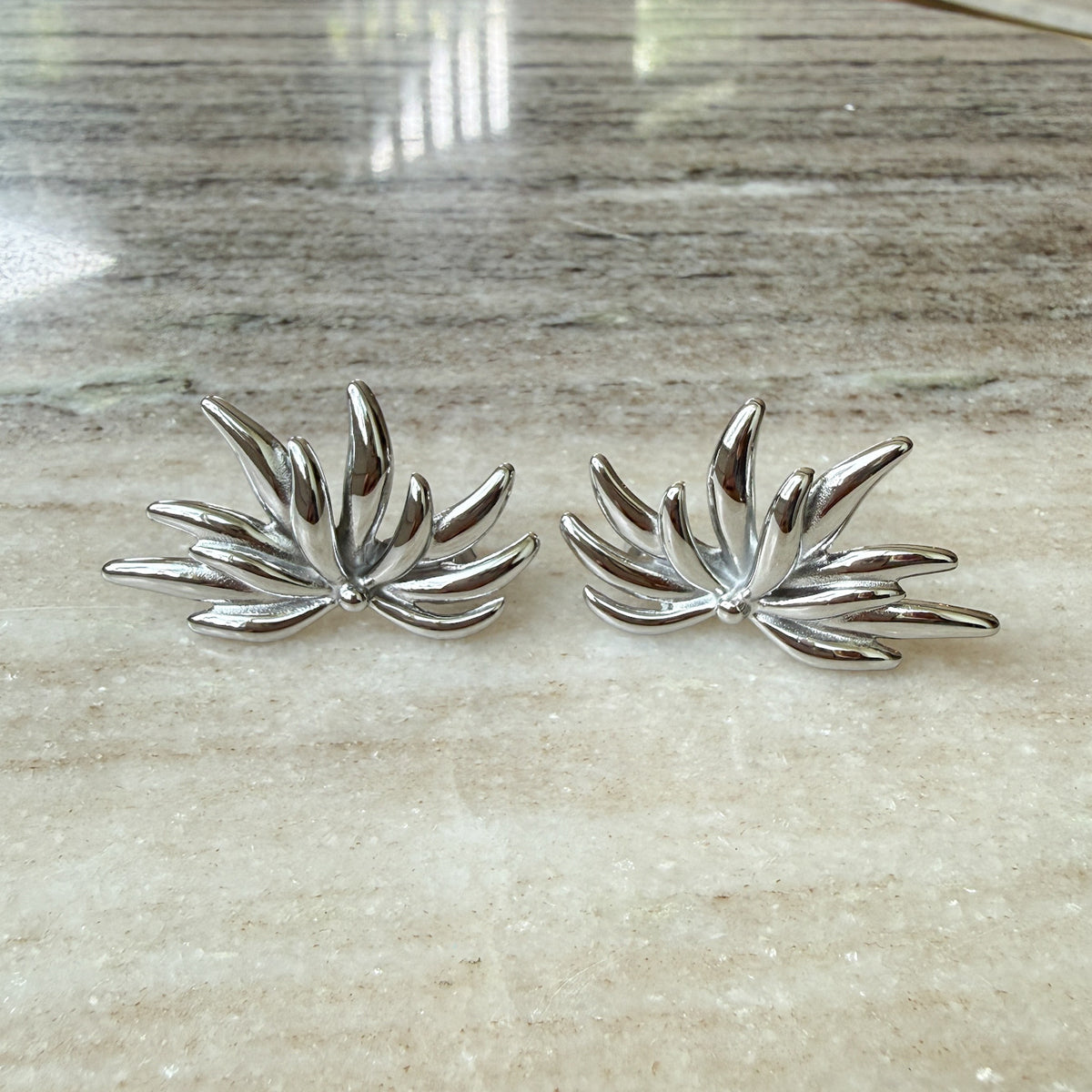Pair of silver leaf-shaped earrings on a marble surface - Fireworks Statement Earrings - The Songbird Collection