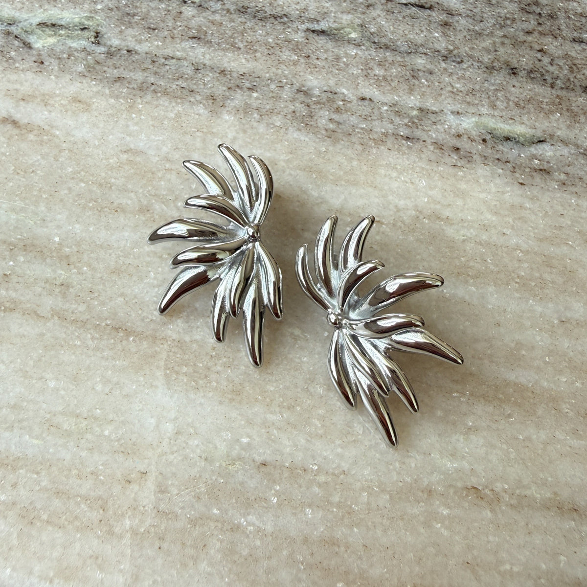 Pair of silver leaf-shaped earrings on a beige stone surface - Fireworks Statement Earrings - The Songbird Collection