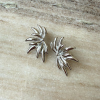 Pair of silver leaf-shaped earrings on a beige stone surface - Fireworks Statement Earrings - The Songbird Collection