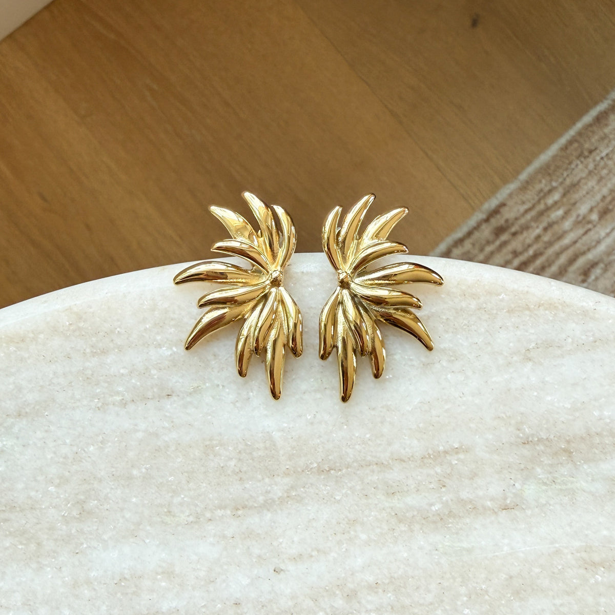 Gold leaf-shaped earrings on a white stone surface with a wooden background